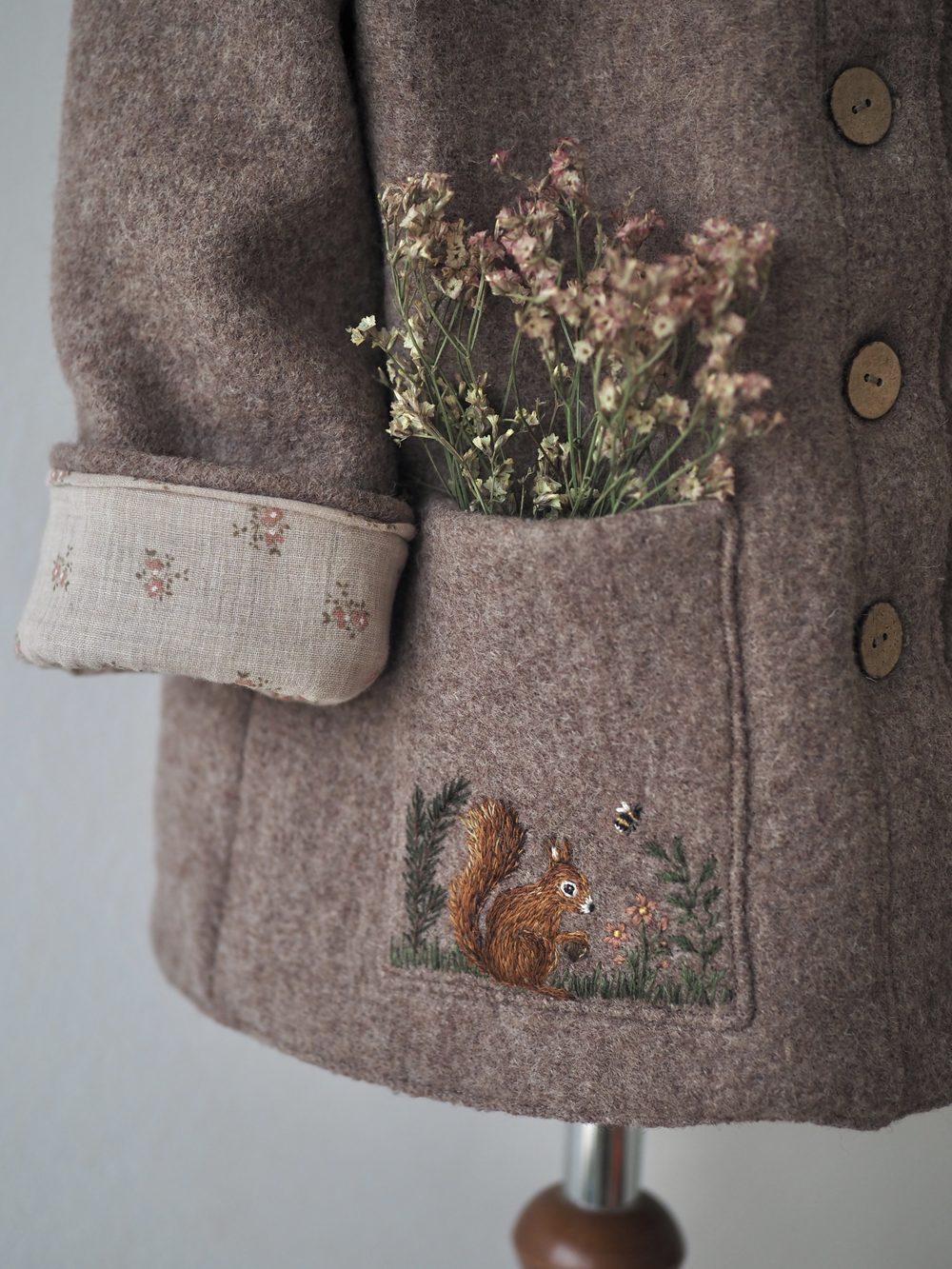 Brauner Wollmantel mit gesticktem Eichhörnchen und Blumen in der Tasche