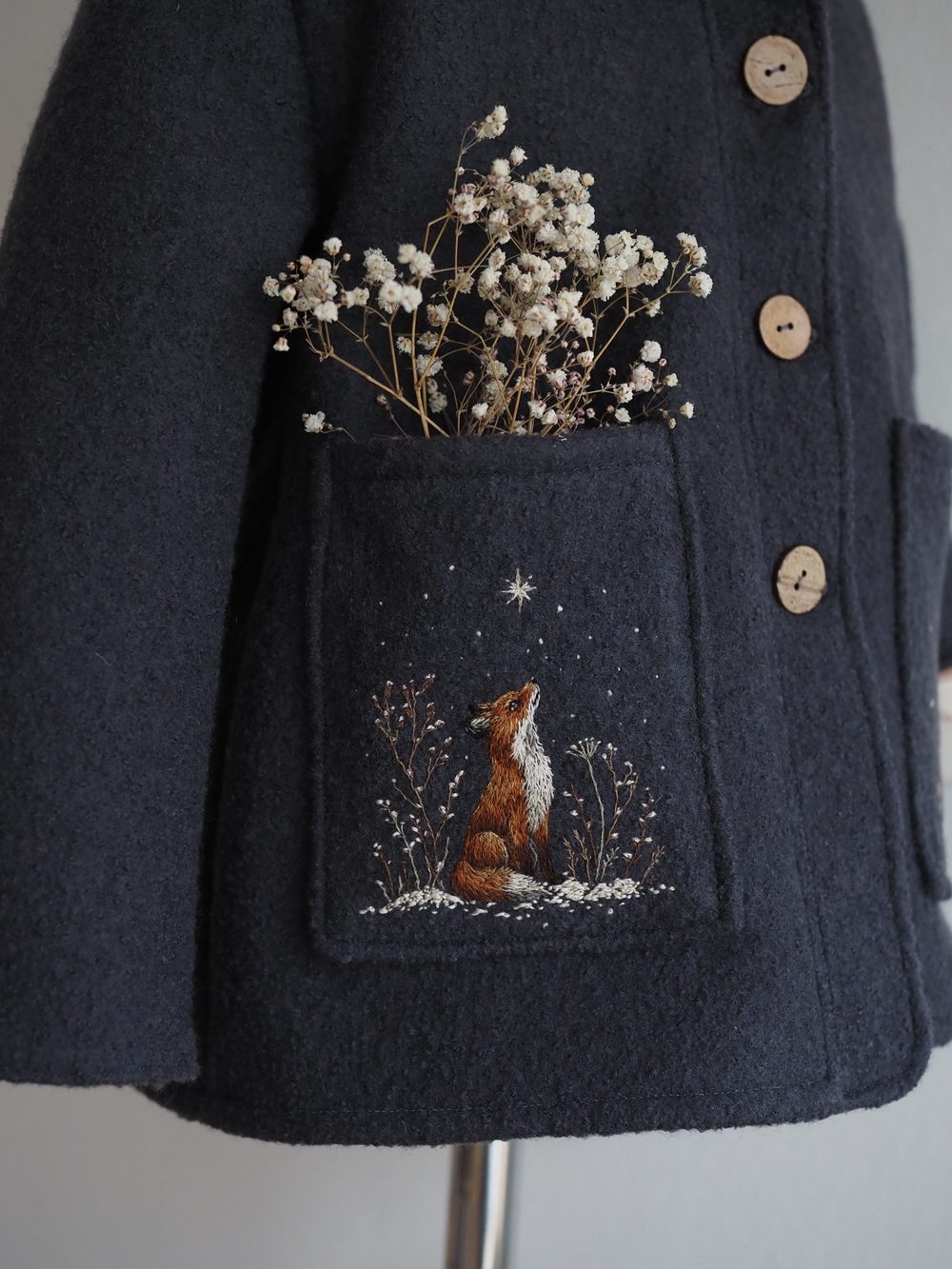 Dunkelblauer Mantel mit gesticktem Fuchs und Schleierkraut in der Tasche