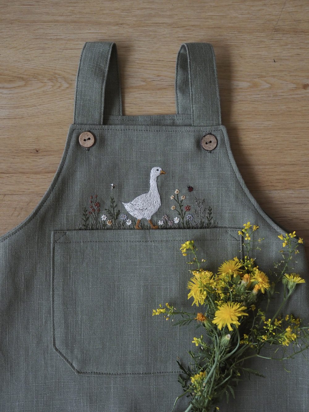 Salbeigrüne Latzhose mit gestickter Gans und Löwenzahn