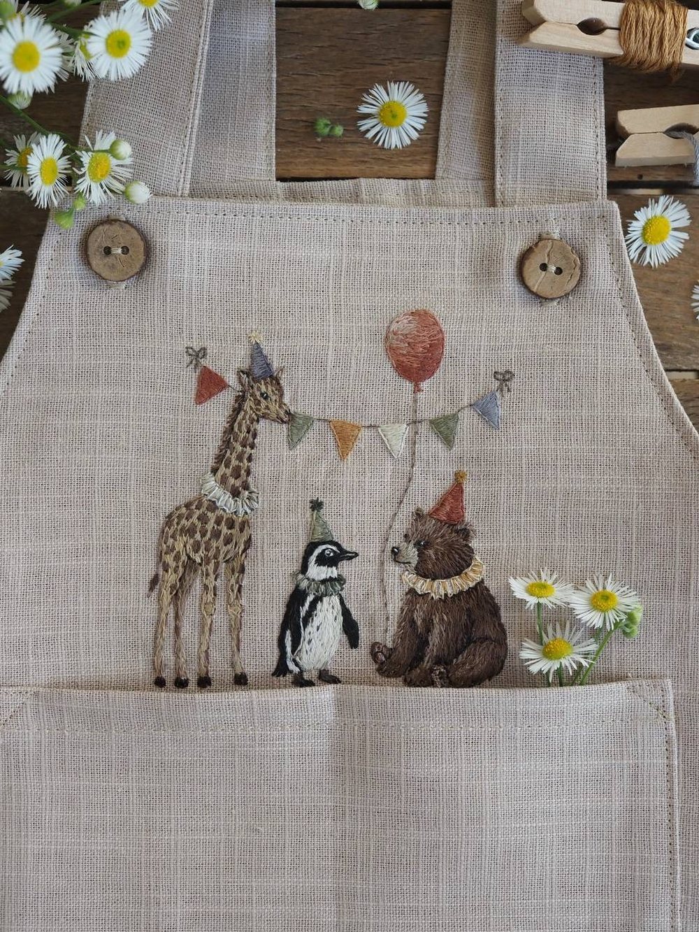 Leinenlatzhose mit gestickter Giraffe, Pinguin und Bär unter einer Wimpelkette