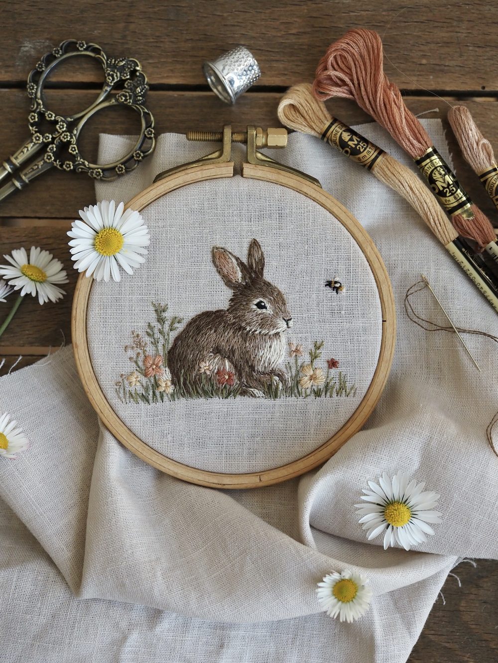 Gestickter Hase im Stickrahmen zwischen Gänseblümchen