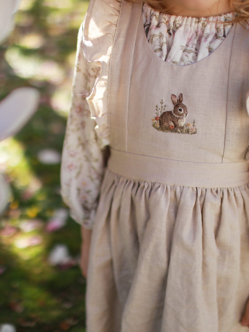 Kind im Kleid mit gesticktem Hasen unter Magnolien