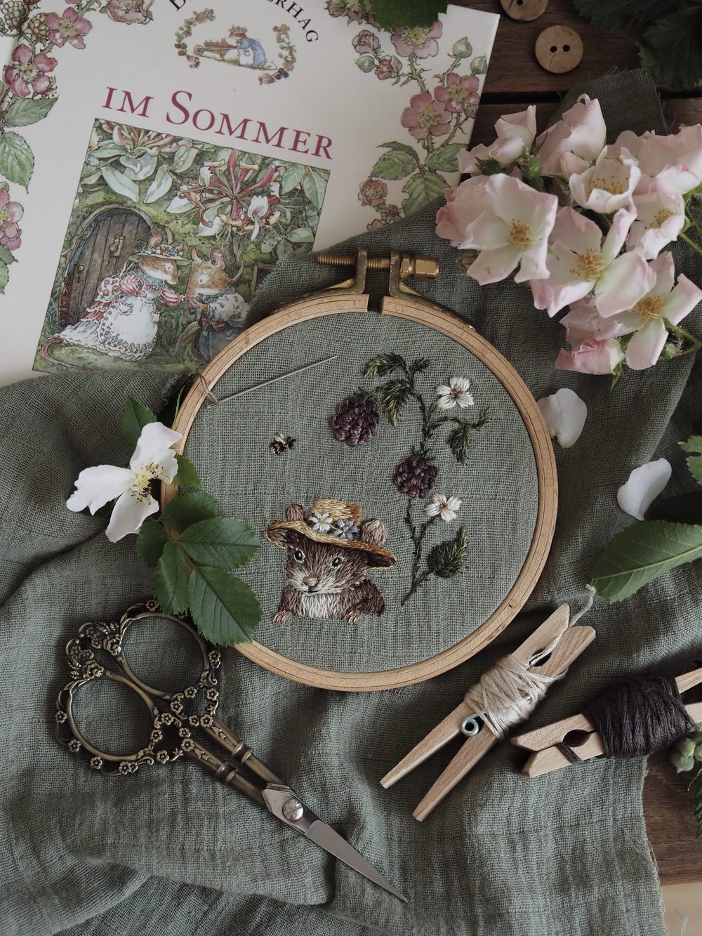 Gestickte Katze mit Strohhut zwischen Brombeeren im Stickrahmen
