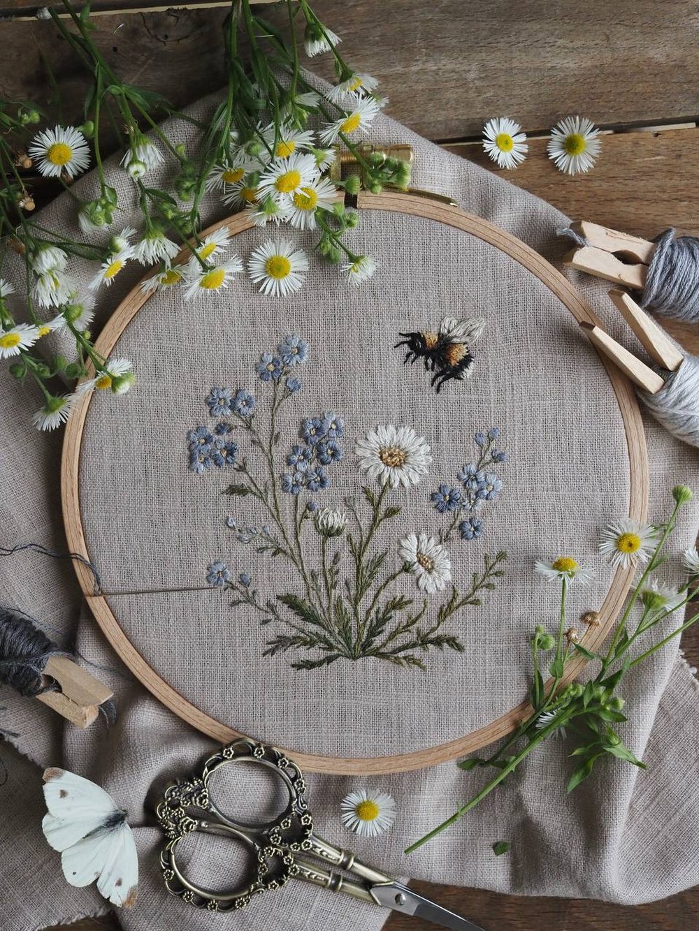 Gestickte Kornblumen und Margeriten mit einer Hummel im Stickrahmen