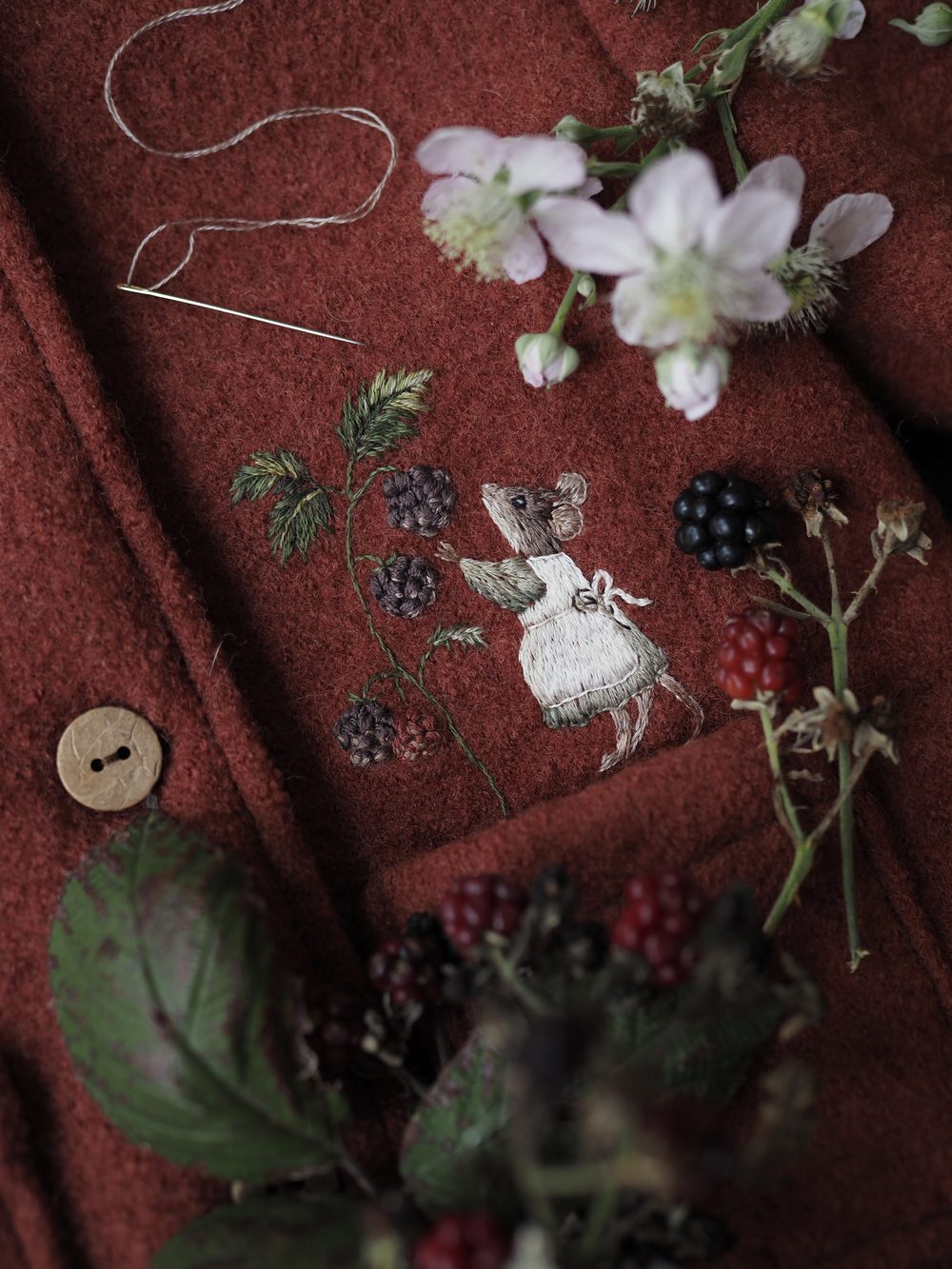 Roter Wollmantel mit gestickter Maus zwischen Brombeeren