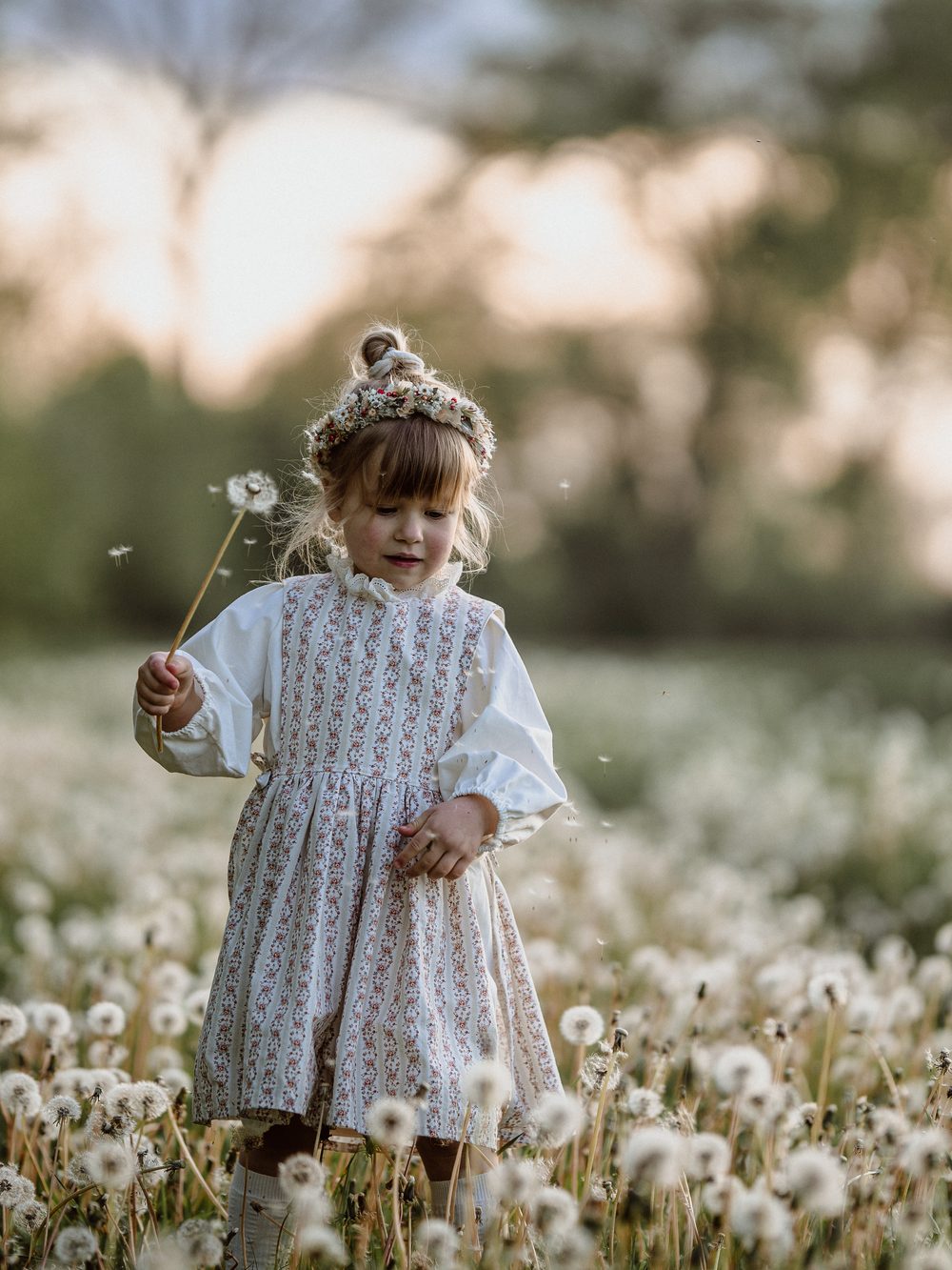 Kind im hellen Kleid in einer Wiese voller Pusteblumen
