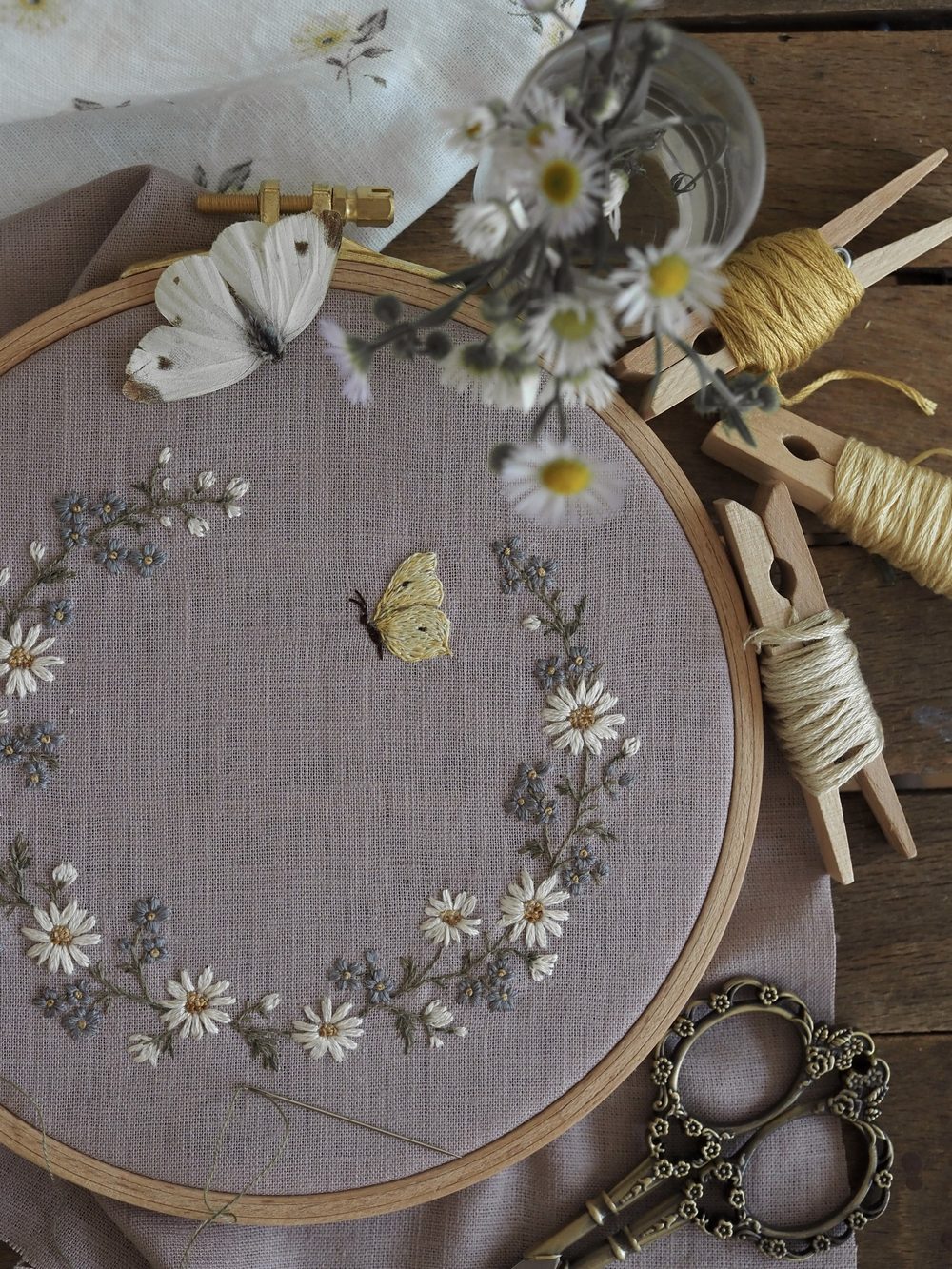 Gestickter Blütenkranz mit Schmetterlingen im Stickrahmen