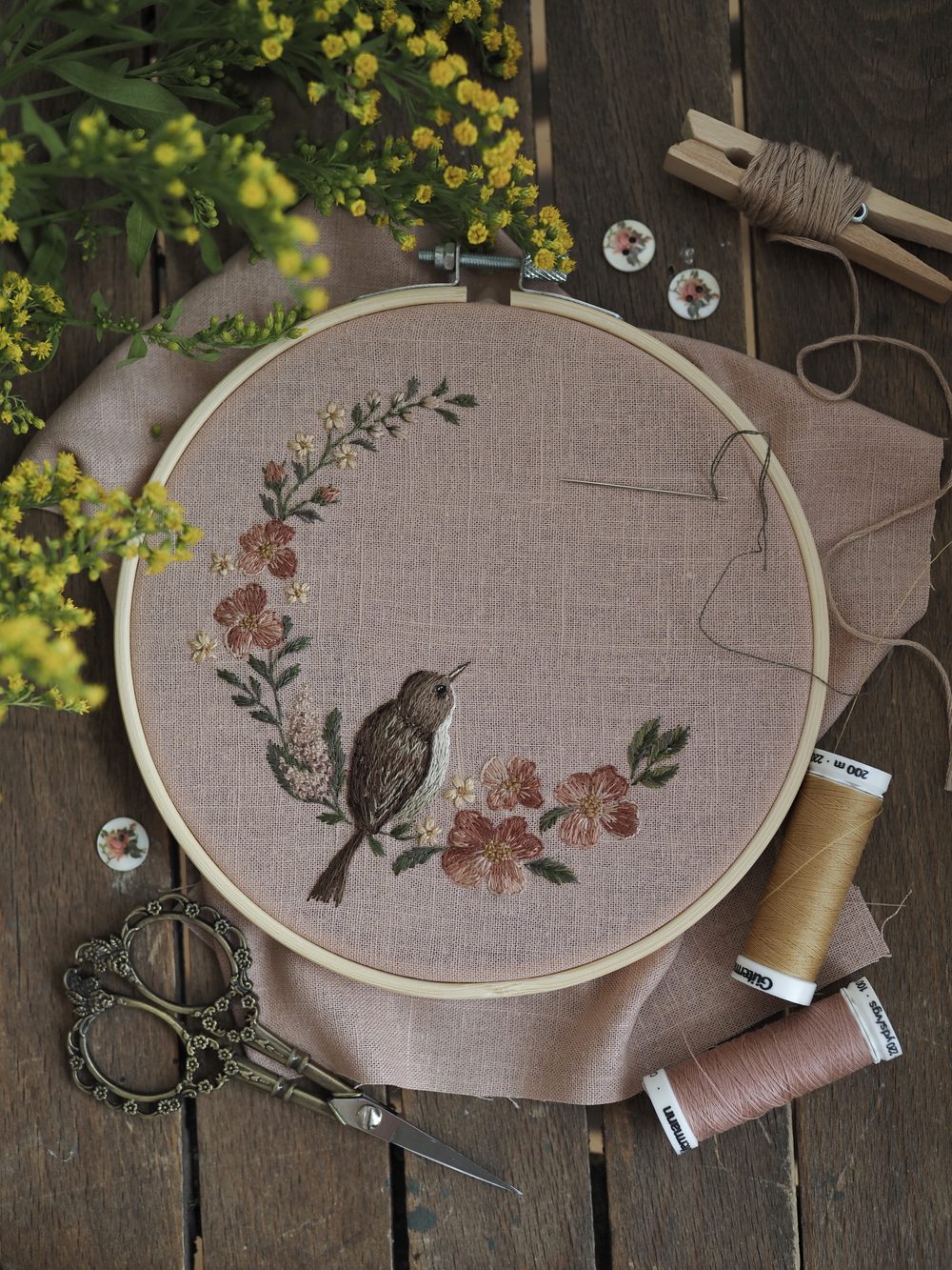 Gestickter Vogel im Blütenkranz auf rosa Leinen