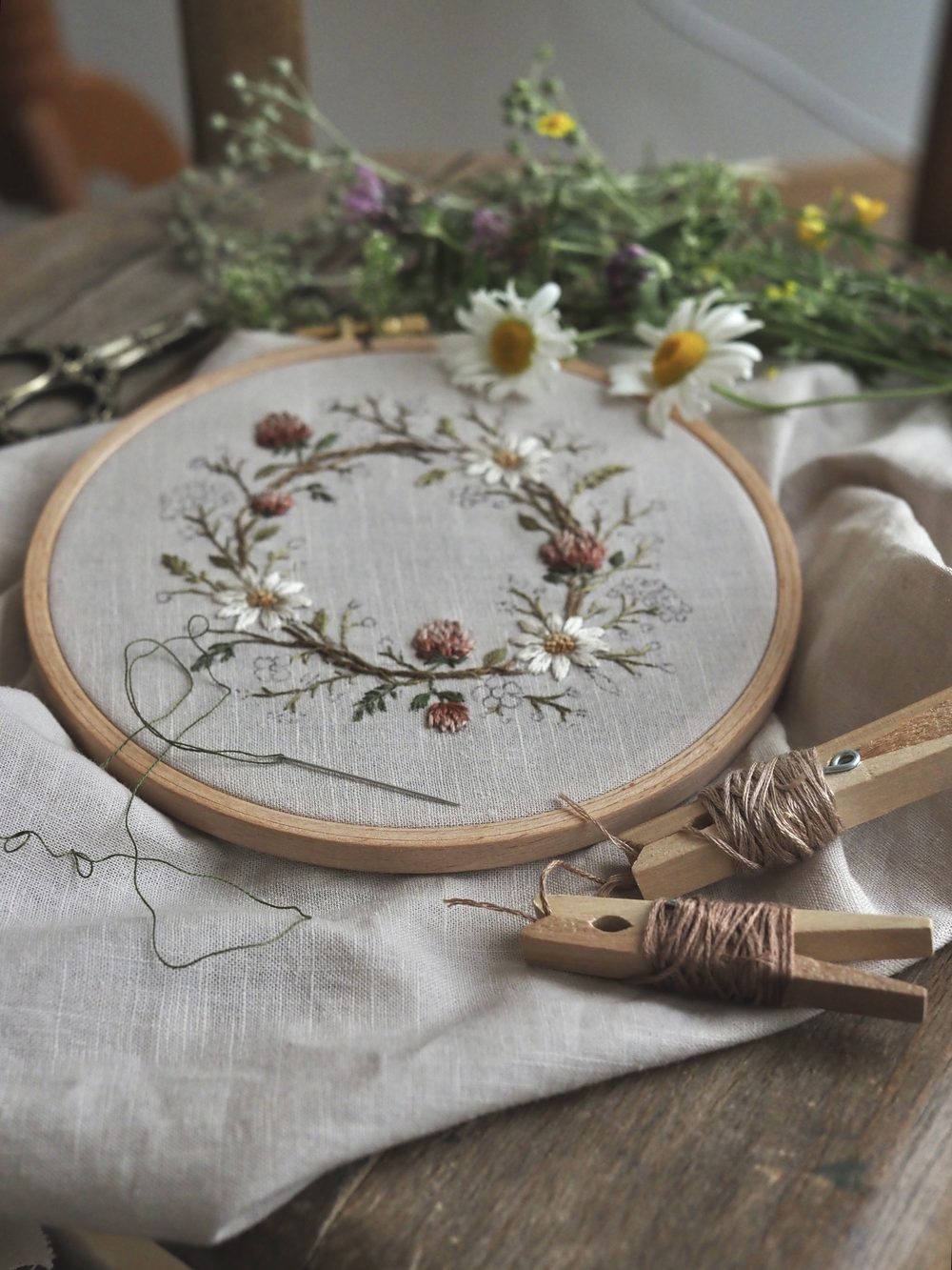 Gestickter Kranz mit Zapfen und Gänseblümchen